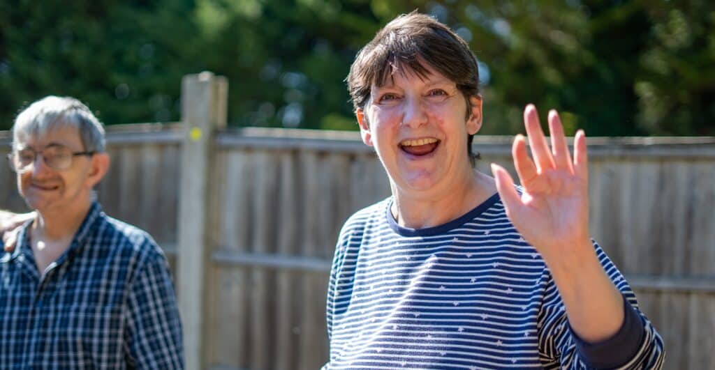 Smiling woman waving while spending time outdoors with another resident in a care home garden.