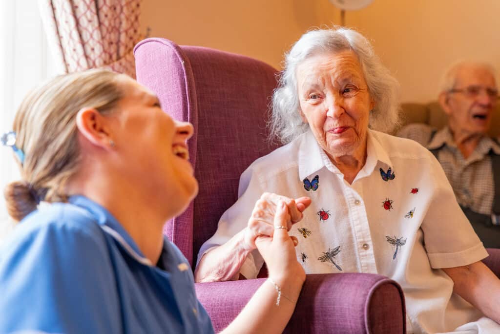 Care team member sharing a warm moment with an older resident in a care home lounge.